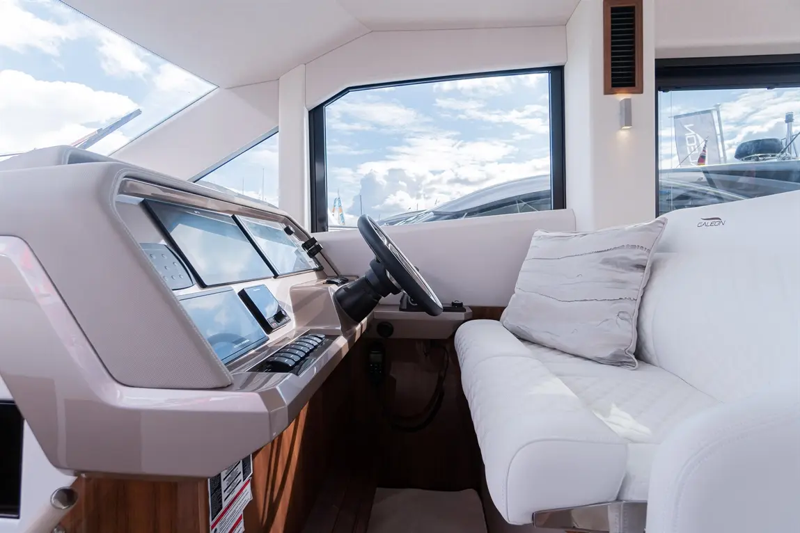 Sleek boat interior showcasing a modern dashboard, steering wheel, and white leather sofa with a cushion, under a bright sky.